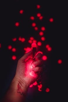 A hand holding glowing red string lights in the dark with a bokeh effect.