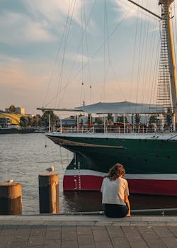 A serene scene of a person by a majestic ship at sunset in Hamburg harbor.