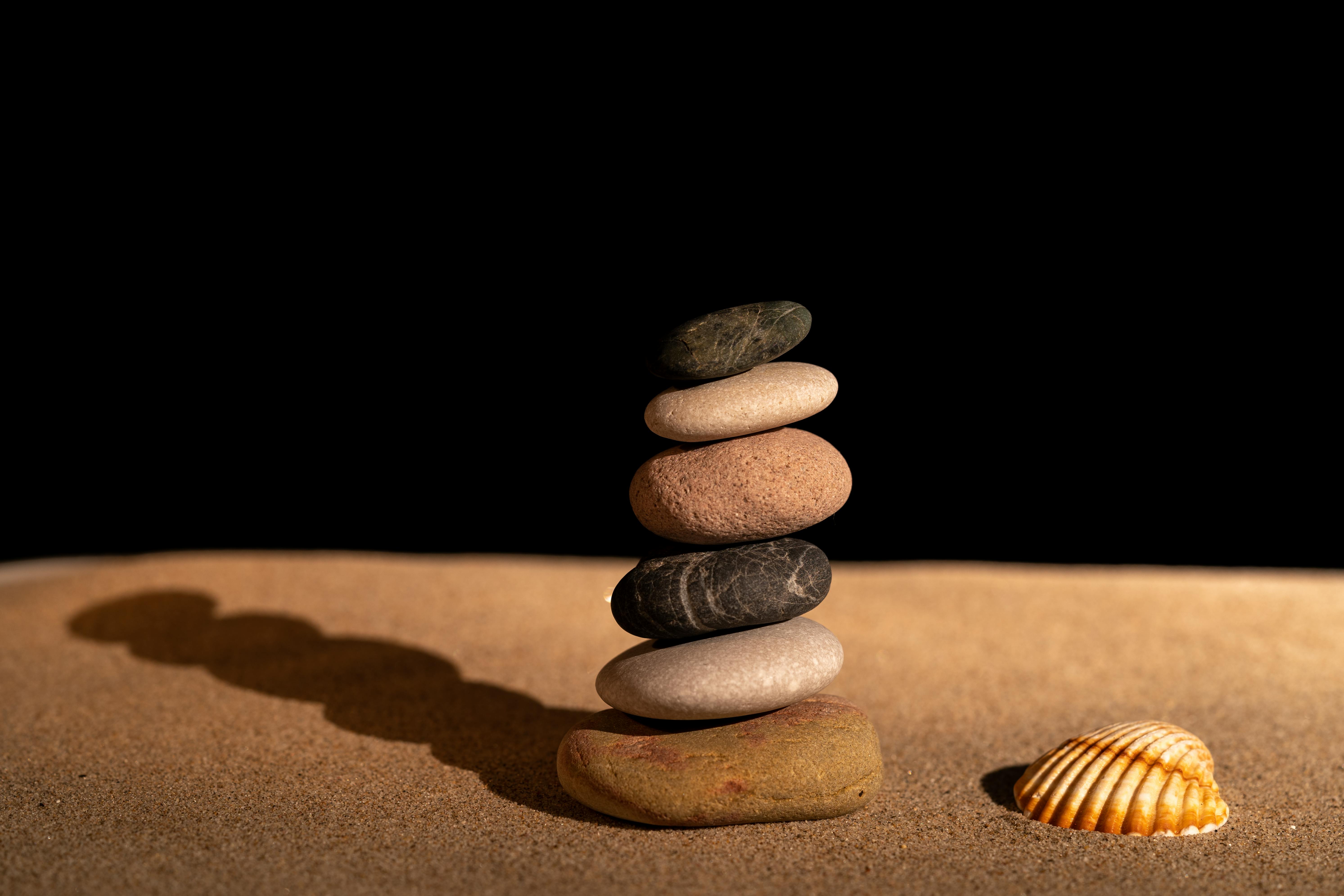 Peaceful zen rock stack with a seashell on a sandy surface, highlighting balance and tranquility.