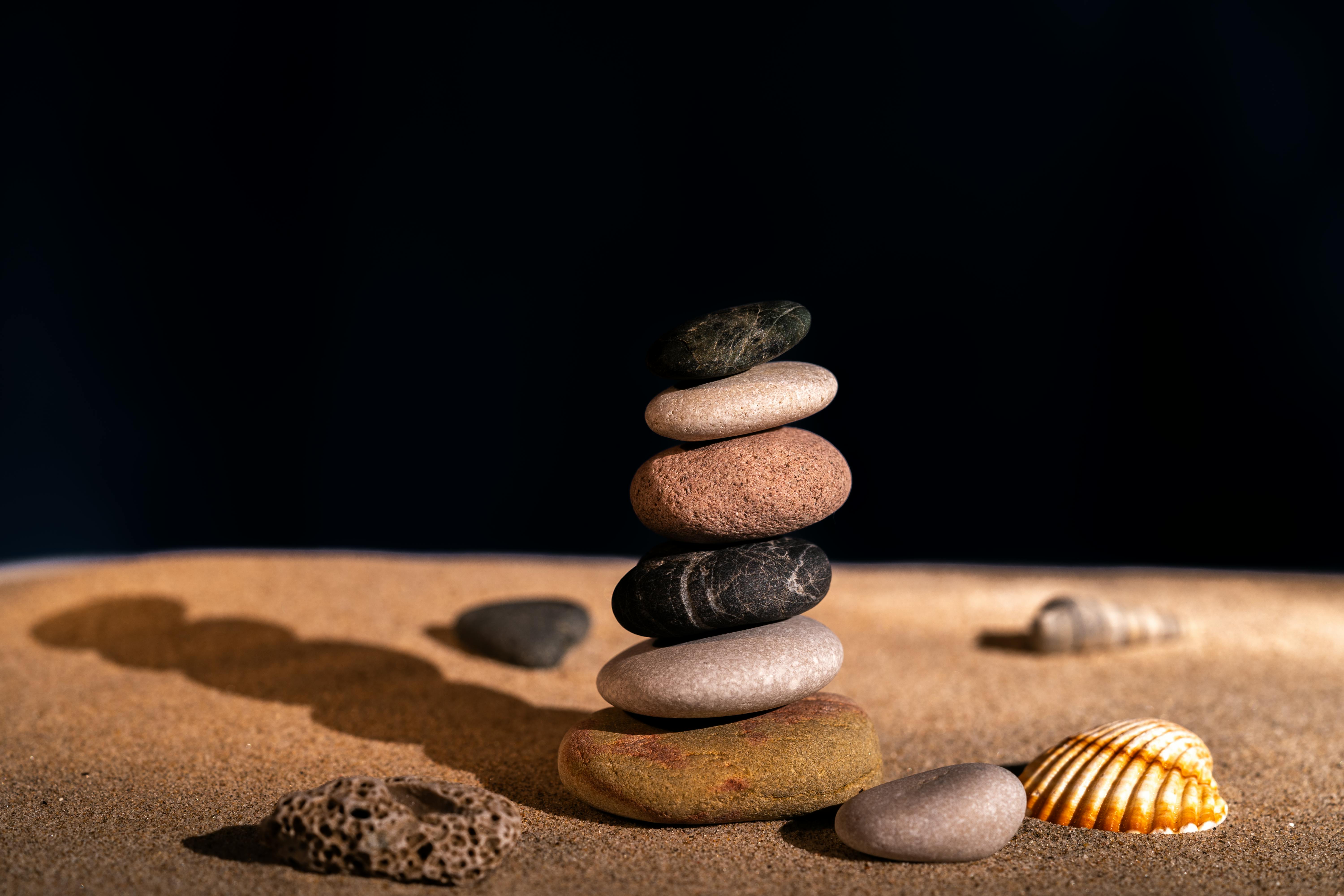 Artistic stack of smooth pebbles on sandy beach with seashells, capturing balance and zen.