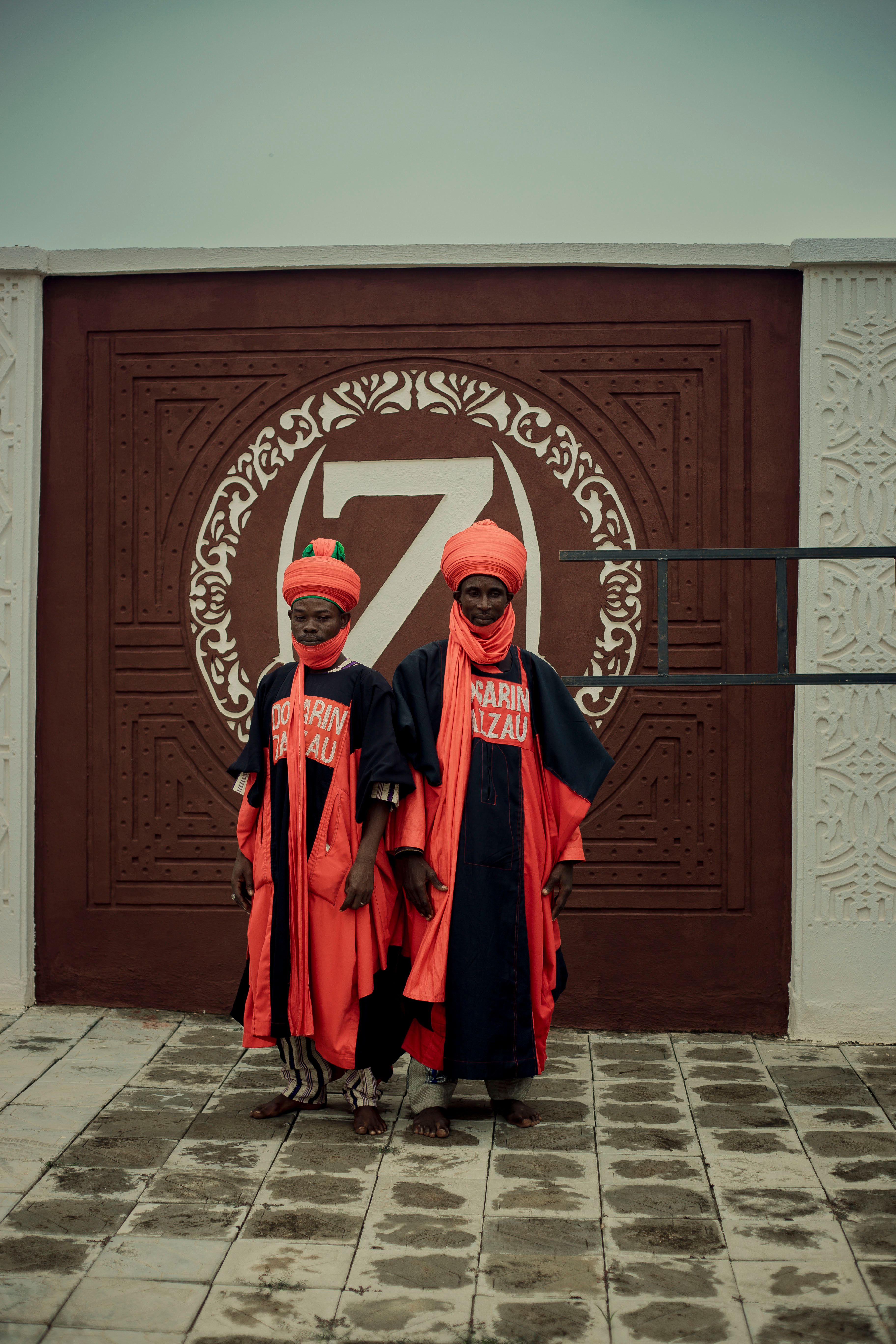 Two individuals in vibrant traditional attire pose before an ornate wall, showcasing cultural heritage.