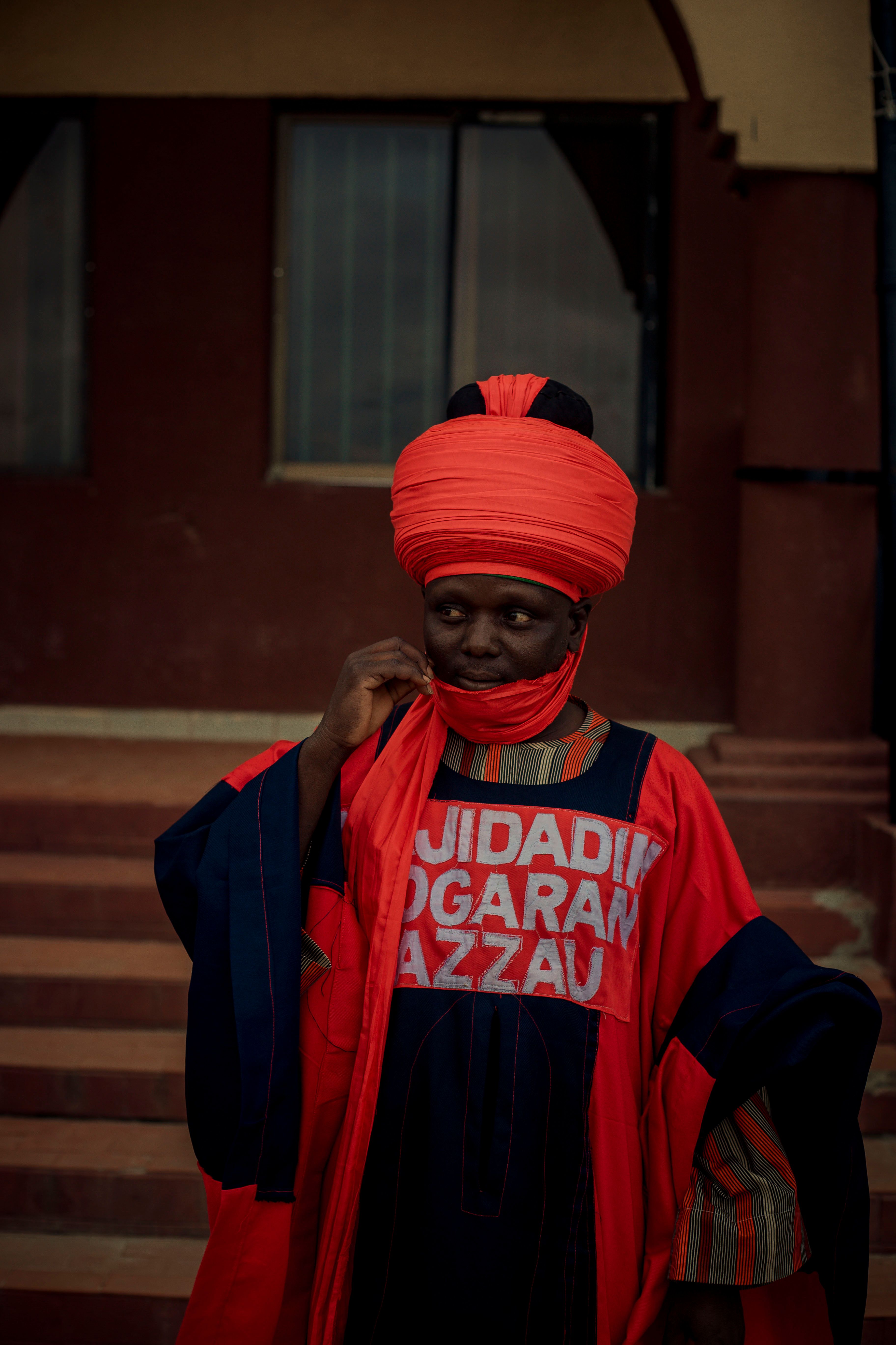 Man in vibrant traditional attire standing outside a building.