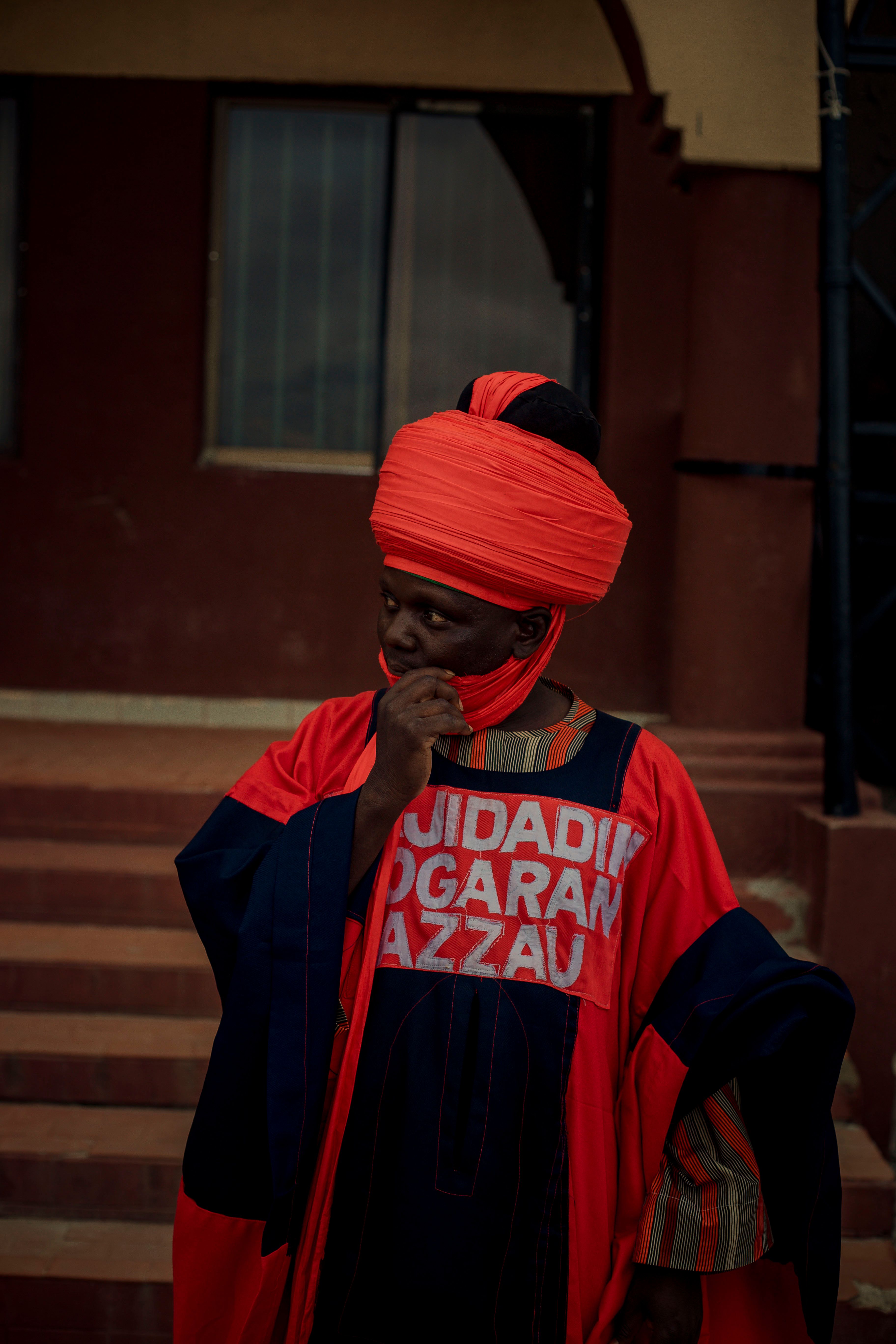 Man in traditional Nigerian attire with a vibrant red turban, exuding cultural elegance.