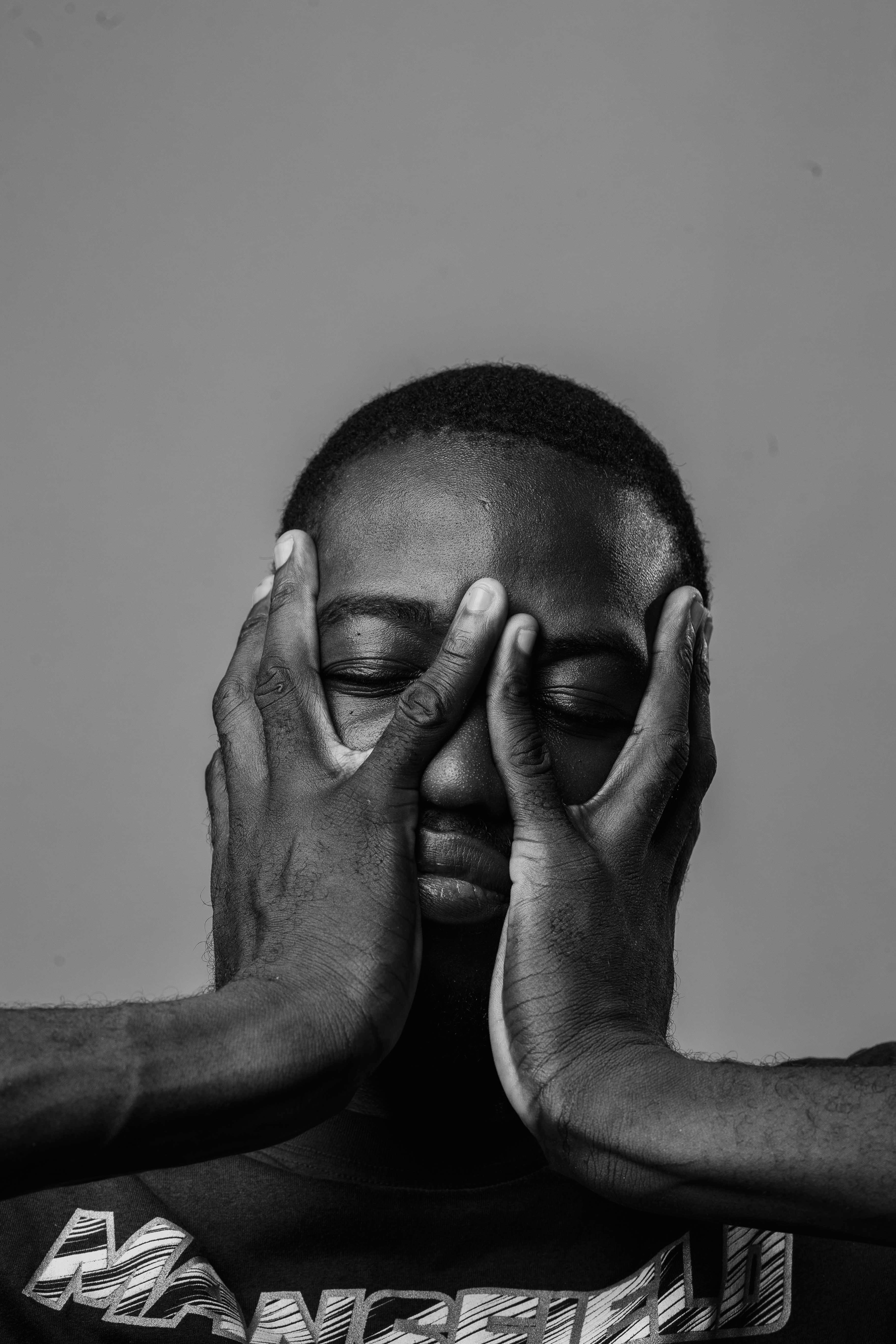 Artistic black and white portrait of young man with hands on face, conveying deep emotions.