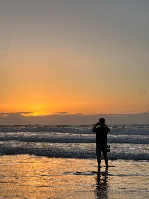 Free Silhouette of a person photographing a beautiful ocean sunset on the beach. Stock Photo