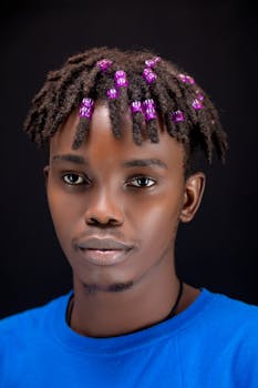 Portrait of a stylish man with beaded dreadlocks and a blue shirt on a black background.