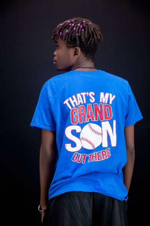 Free Teenager wearing a blue T-shirt with baseball-themed print, standing against dark background. Stock Photo