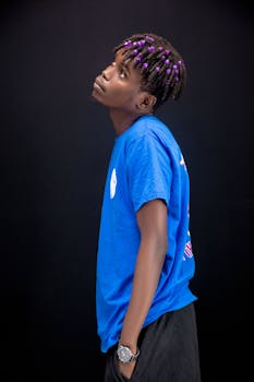 Stylish young adult with purple accented hair posing against a black background, showcasing modern fashion vibes.