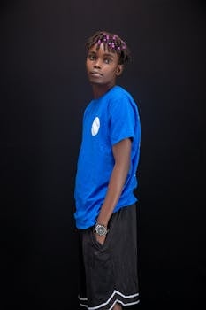 Stylish young man in blue shirt posing confidently against a black background.