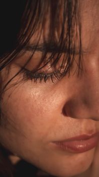An intimate close-up portrait of a woman with closed eyes and soft lighting highlighting her features.