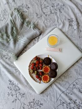 A cozy flat lay scene with desserts, skincare, and a laptop on patterned bedding.