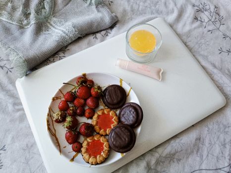 A cozy indoor scene featuring a plate of strawberries and cookies, alongside a glass of juice on a tray.