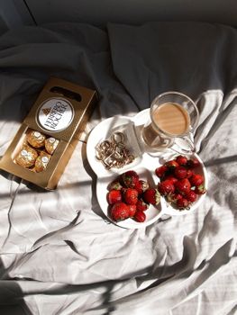 Delightful morning setup featuring coffee, strawberries, and chocolates on a bed.