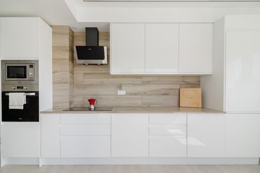 Sleek white minimalistic kitchen with modern appliances and wooden accents.
