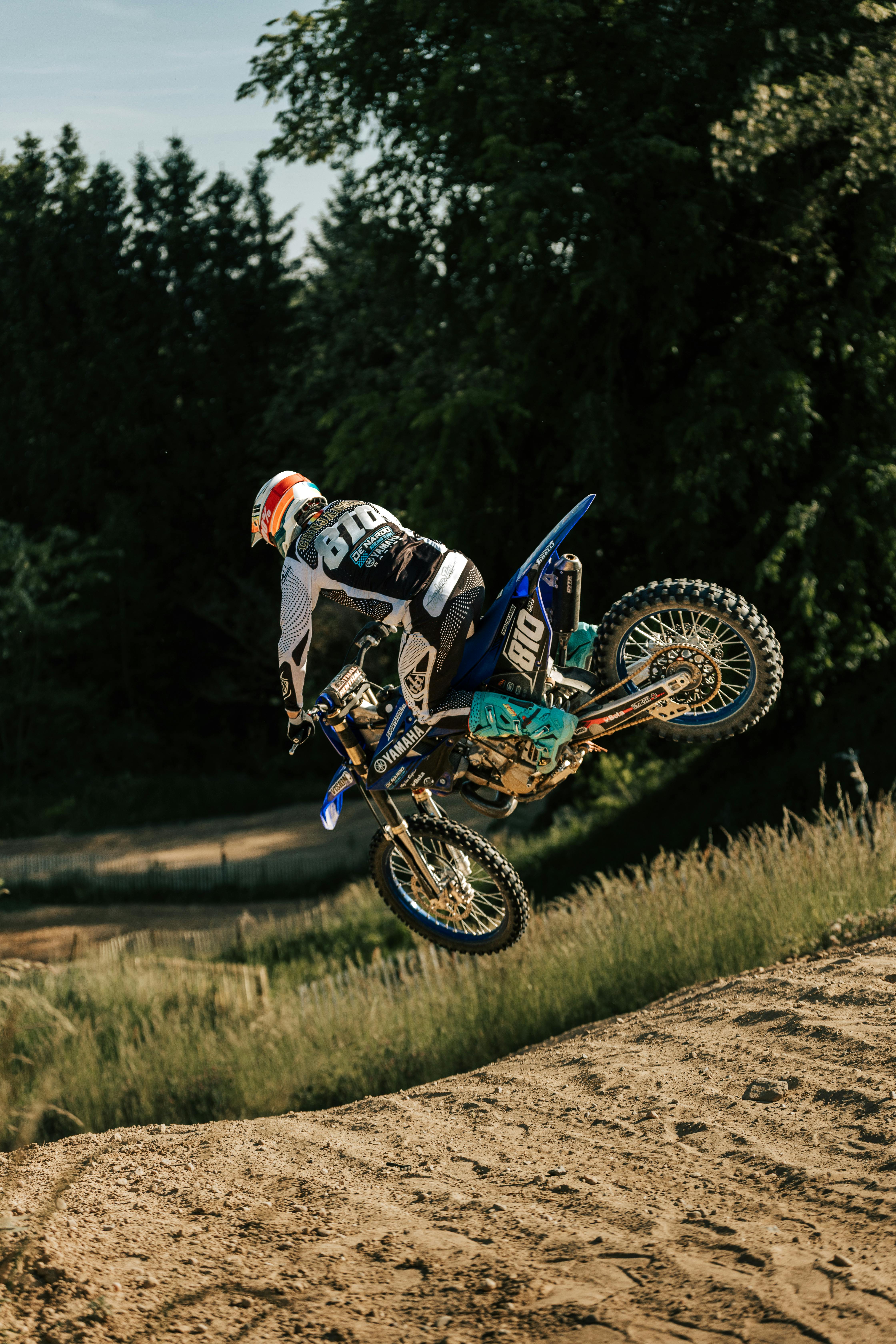 Exciting motocross action jump captured on a dirt track amidst nature.