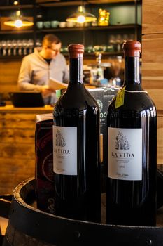 Two wine bottles labeled 'La Vida' on a barrel in a warm, cozy café environment with a blurred background.