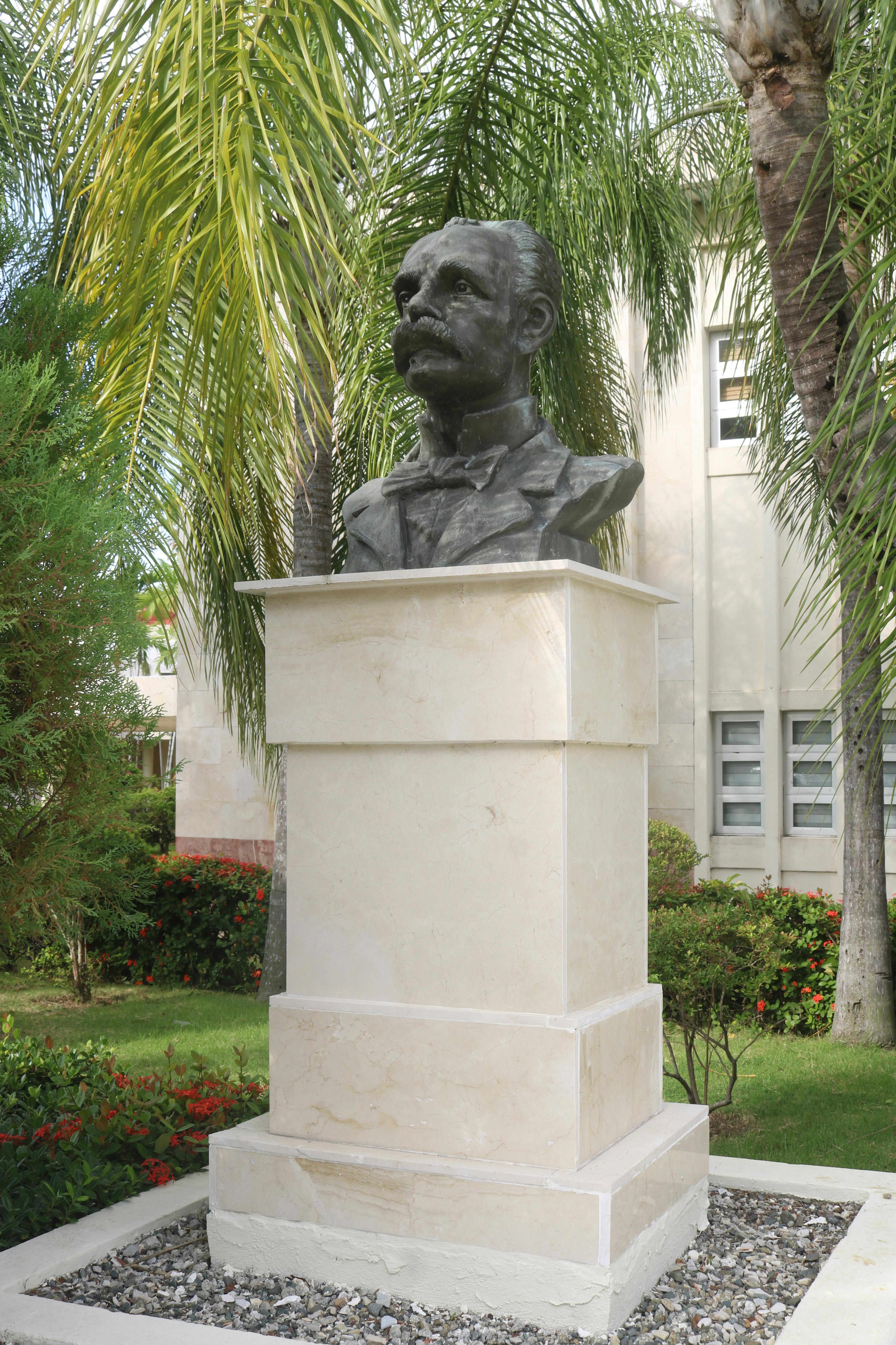 Bronze bust monument in a lush garden with palm trees.