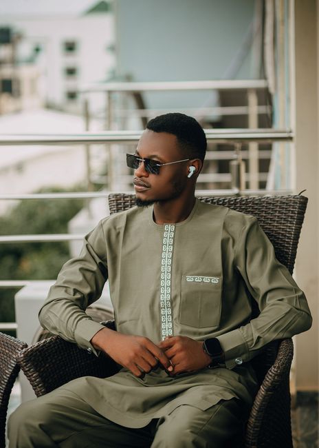 Portrait of a fashionable man in traditional attire wearing sunglasses, relaxing outdoors.