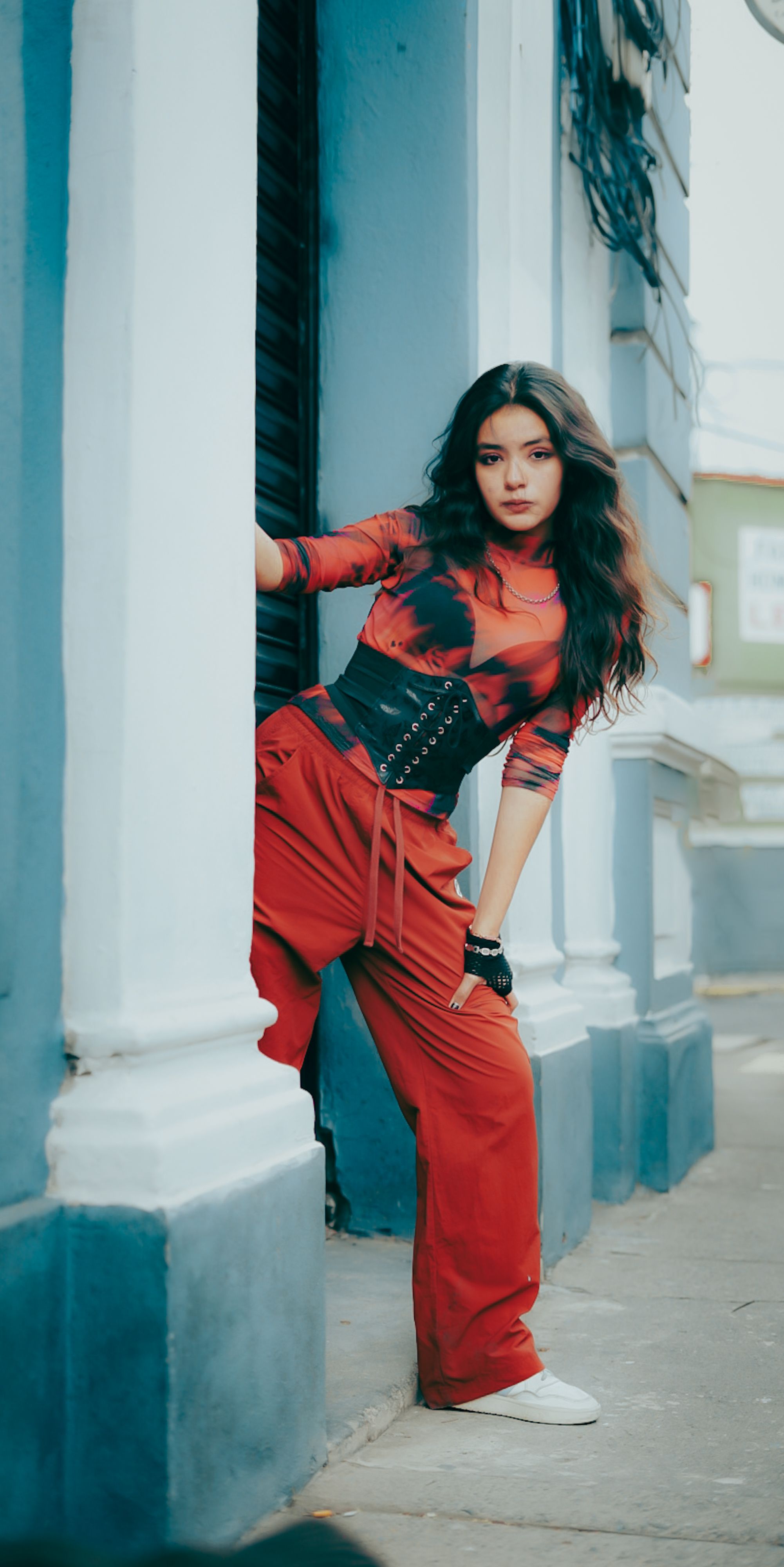 Stylish woman in red outfit leaning against a building in a city street setting.