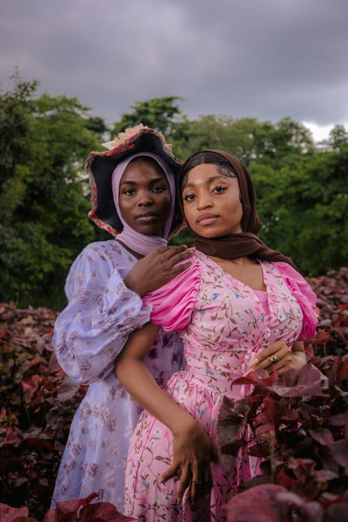 Free Two women wearing floral dresses pose gracefully amidst vibrant foliage. Stock Photo