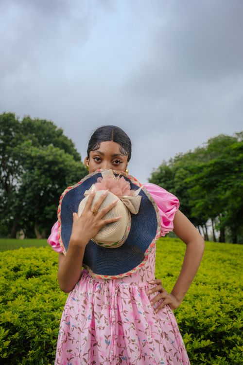 Free A woman in a pink dress holding a hat against a green landscape in Nigeria. Stock Photo