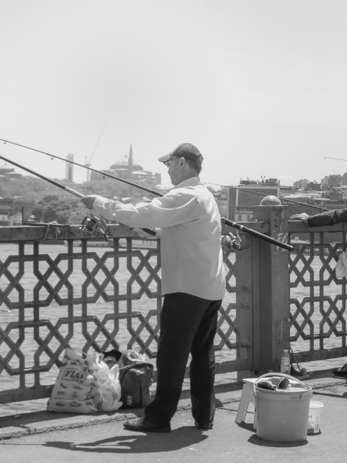Free Black and white photo of a man fishing from the Galata Bridge in Istanbul on a sunny day. Stock Photo