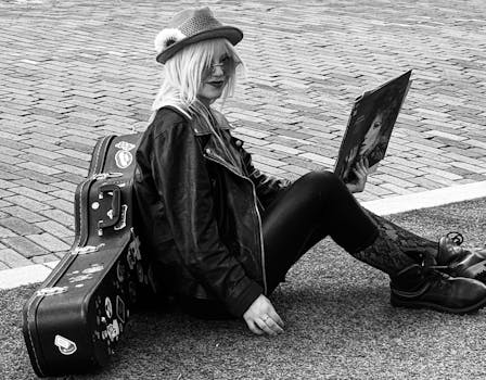 A fashionable woman in leather reads a vinyl record, sitting by a guitar case in Orlando.
