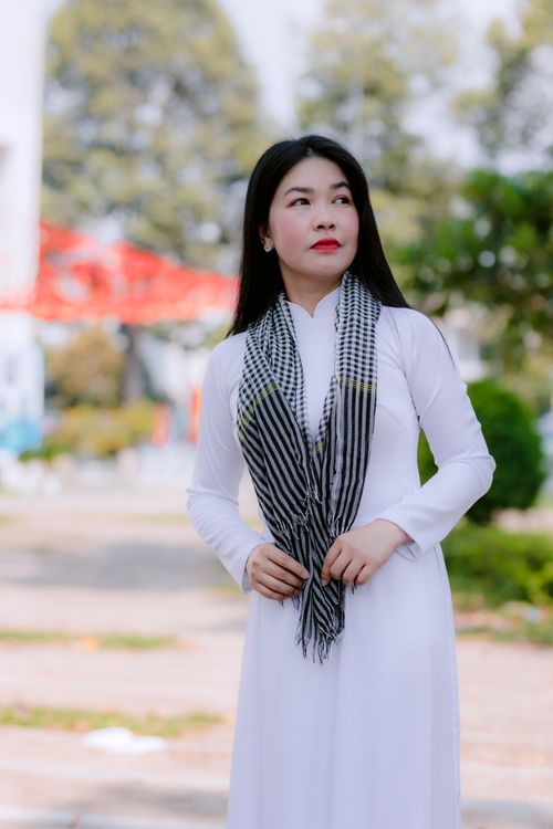 Free Asian woman in white dress and scarf standing outdoors, looking confidently. Stock Photo