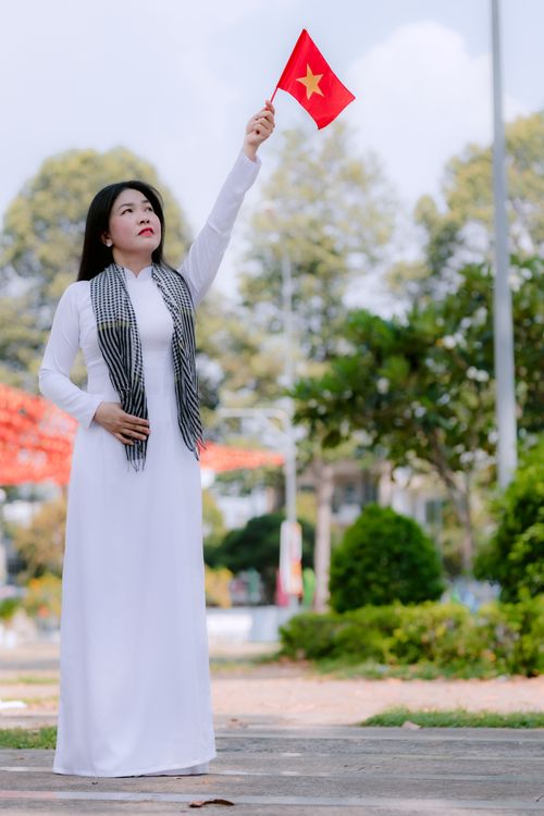 Free Elegant Vietnamese woman in traditional attire waving the national flag outdoors. Stock Photo