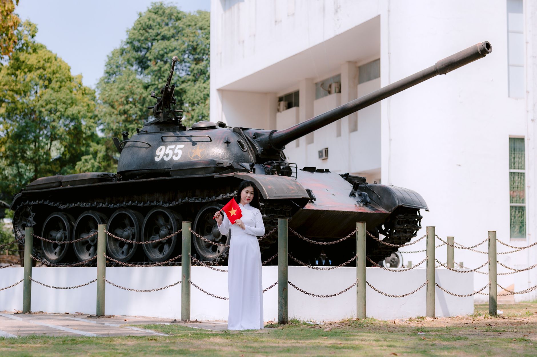 Young woman holding national flag near military tank outdoors, bright day.