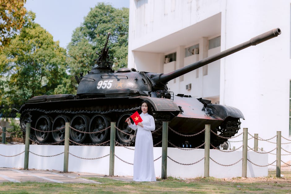 Woman in traditional dress holding Vietnam flag near tank outdoors.