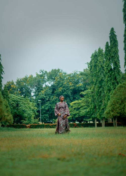 Free A serene image of a woman in traditional clothing standing amidst lush greenery in a park. Stock Photo