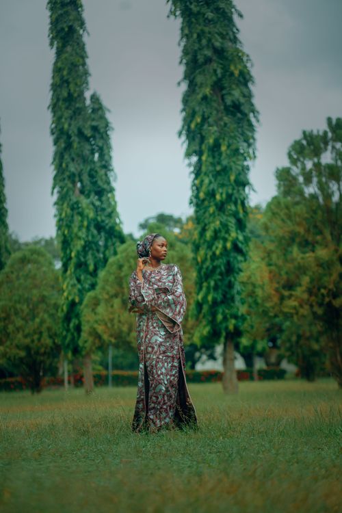 Free A woman in traditional attire stands gracefully in a green park surrounded by tall trees. Stock Photo