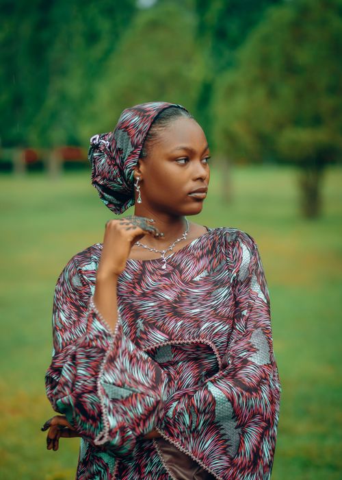 Free Stylish young woman in vibrant African dress posing in a lush green park. Stock Photo