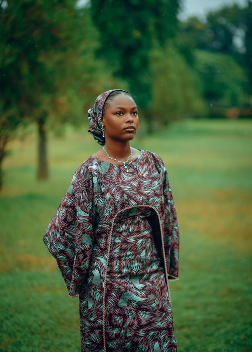 Free Portrait of an elegant woman wearing vibrant traditional African attire standing outdoors in a lush green garden. Stock Photo