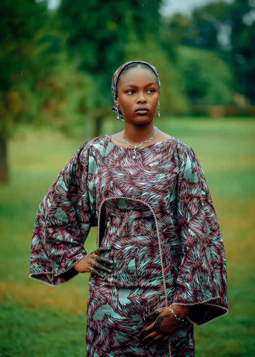 Free Portrait of an African woman in colorful traditional attire standing in a lush green park. Stock Photo