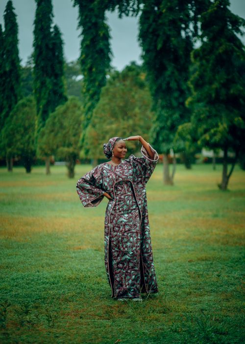 Free A woman in colorful traditional African attire poses gracefully in a lush green park. Stock Photo