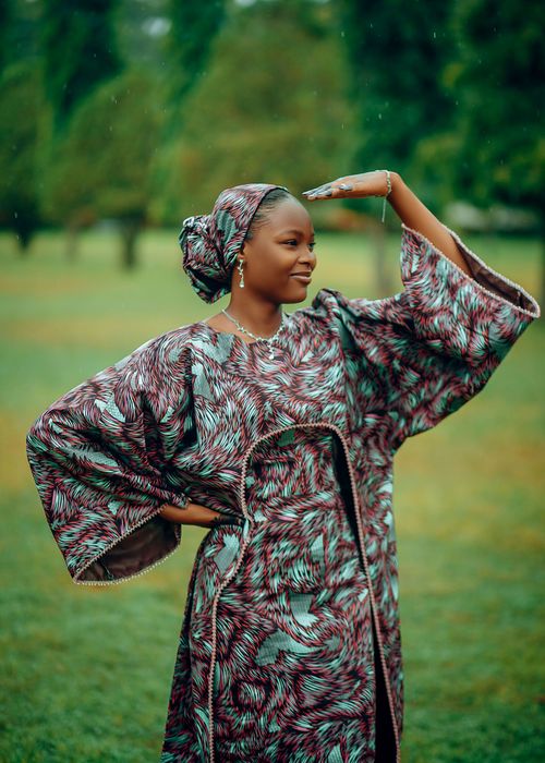 Free A woman in vibrant African traditional dress poses gracefully in a lush outdoor setting. Stock Photo