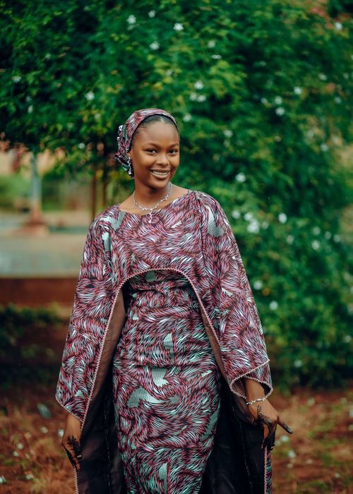 Free Joyful woman in vibrant traditional attire smiling in a lush green outdoor setting. Stock Photo