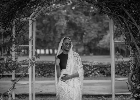 Black and white portrait of a woman in traditional attire standing in a garden archway.
