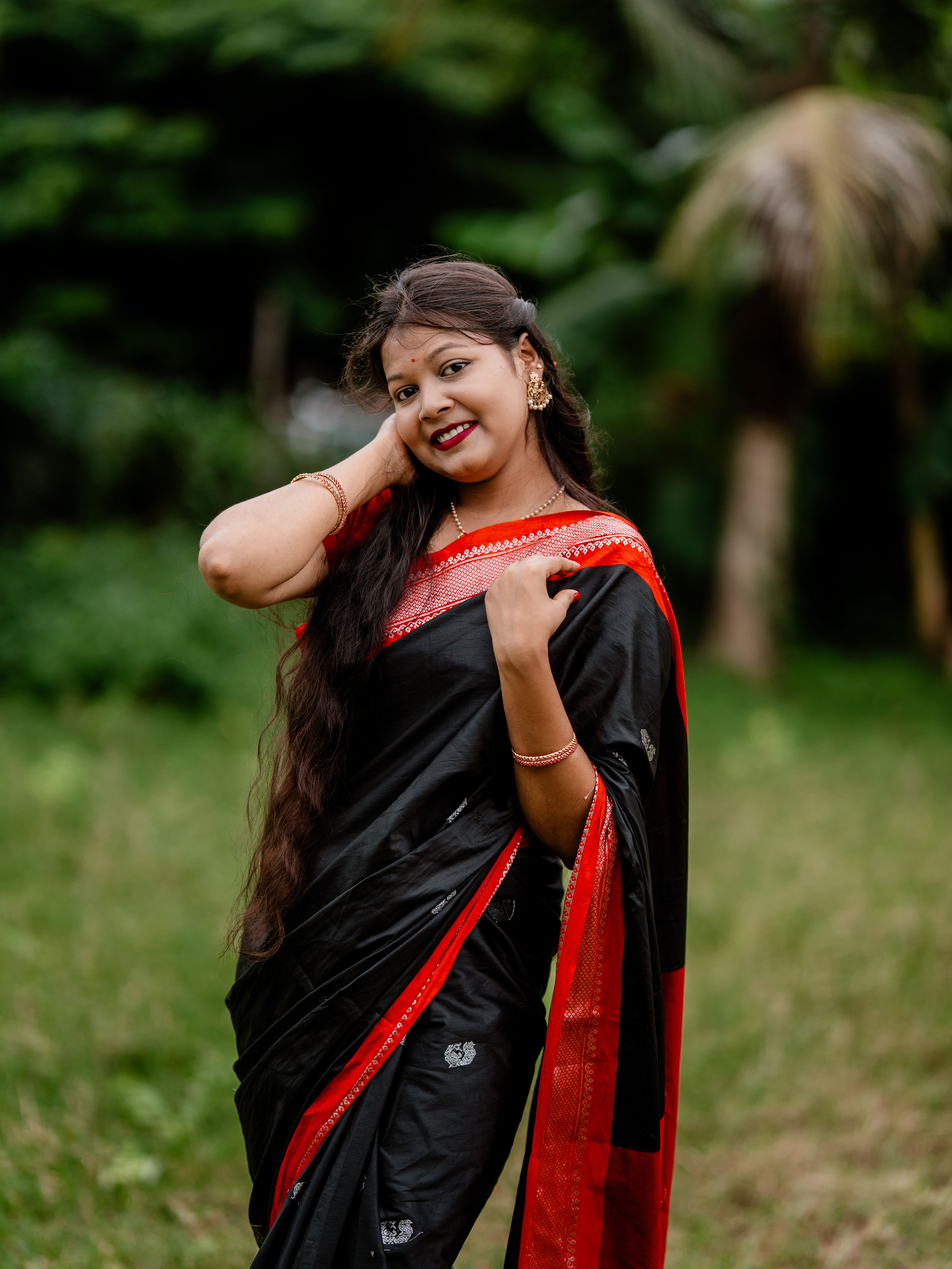 Portrait of a smiling Indian woman in a black saree, showcasing traditional jewelry and fashion.