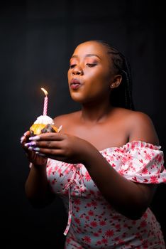 Woman celebrating birthday by blowing out candle on cupcake with joyful expression.