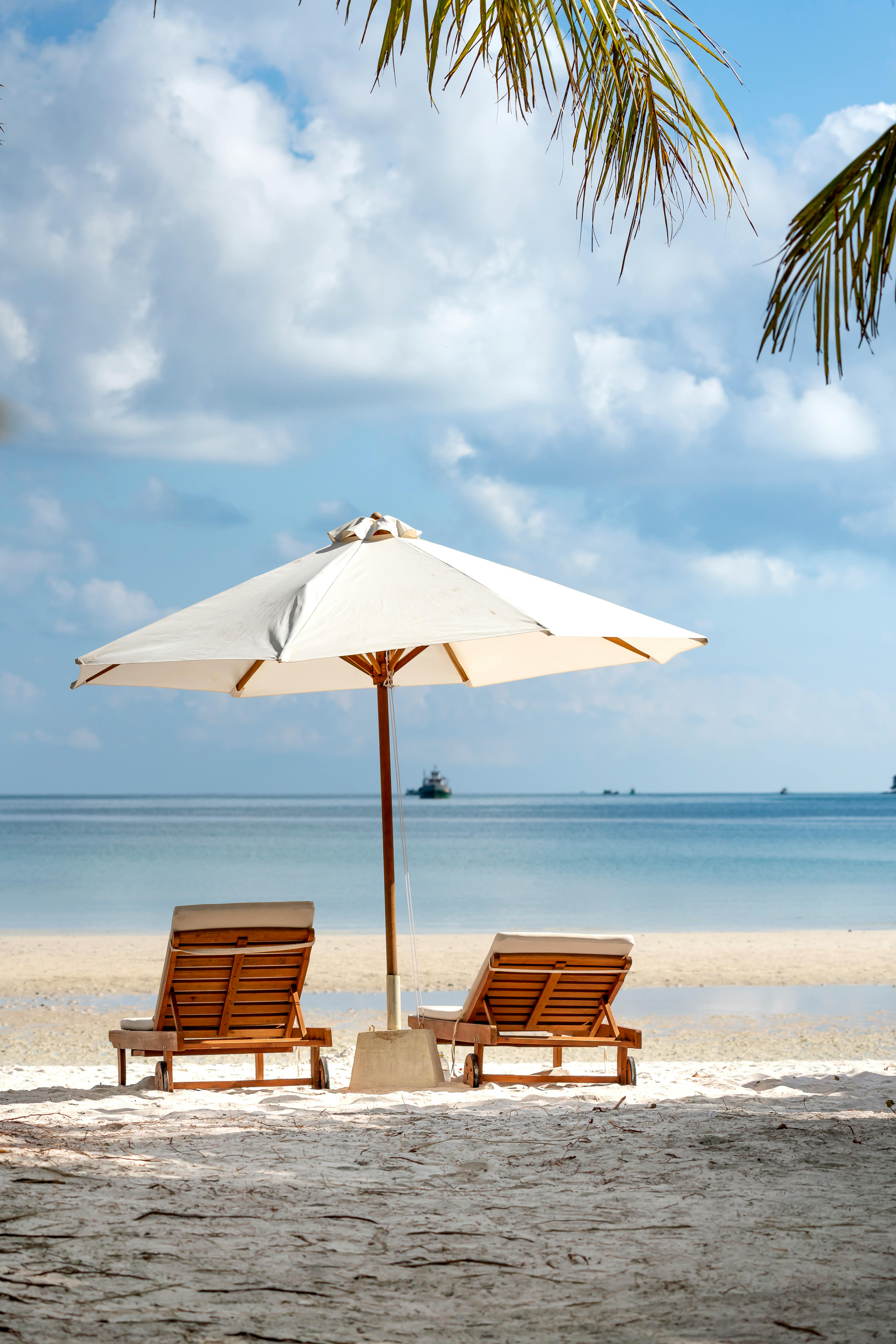 two brown wooden armchairs beside umbrella near seashore