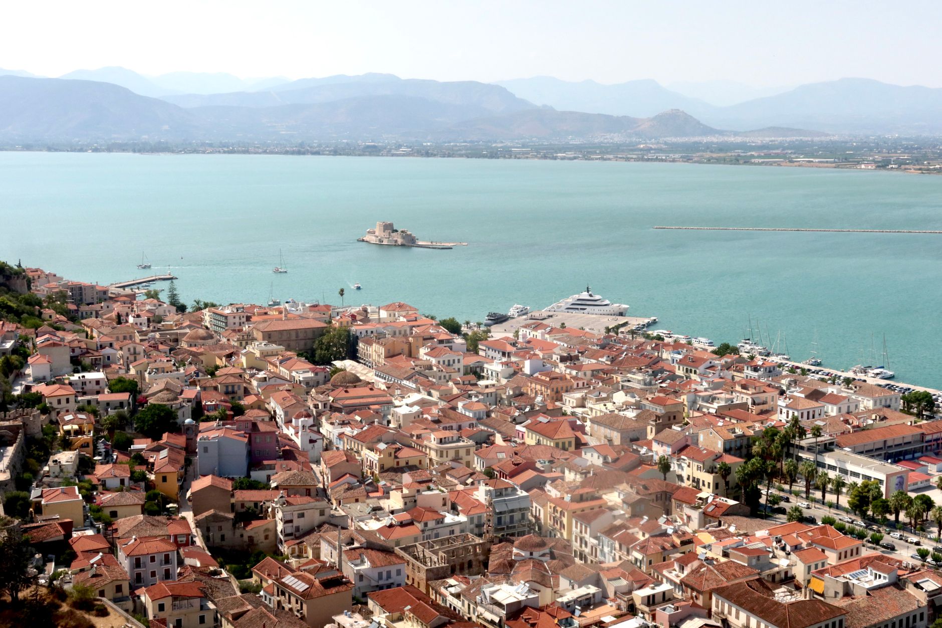 Small boats moored in the circular Venetian harbour of Nafpaktos with the hillside castle rising behind.