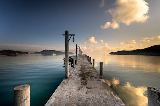 A peaceful pier leading into the ocean, captured during golden hour against a soft, cloudy sky.