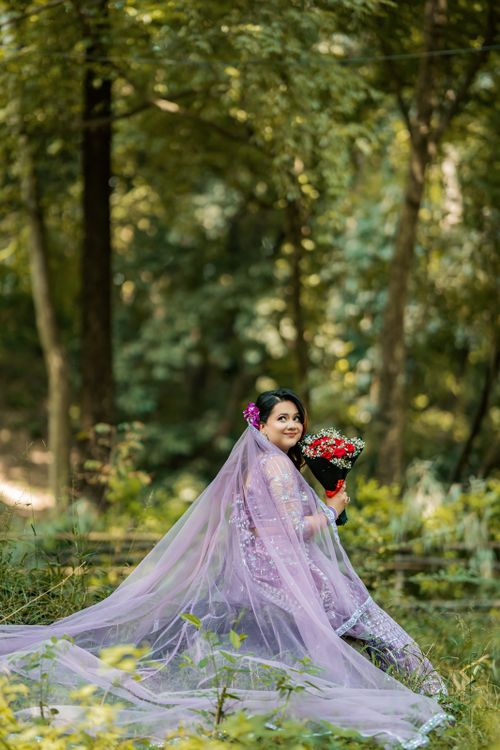 Free Elegant woman in a lavender gown holding flowers, sitting in a serene forest setting. Stock Photo
