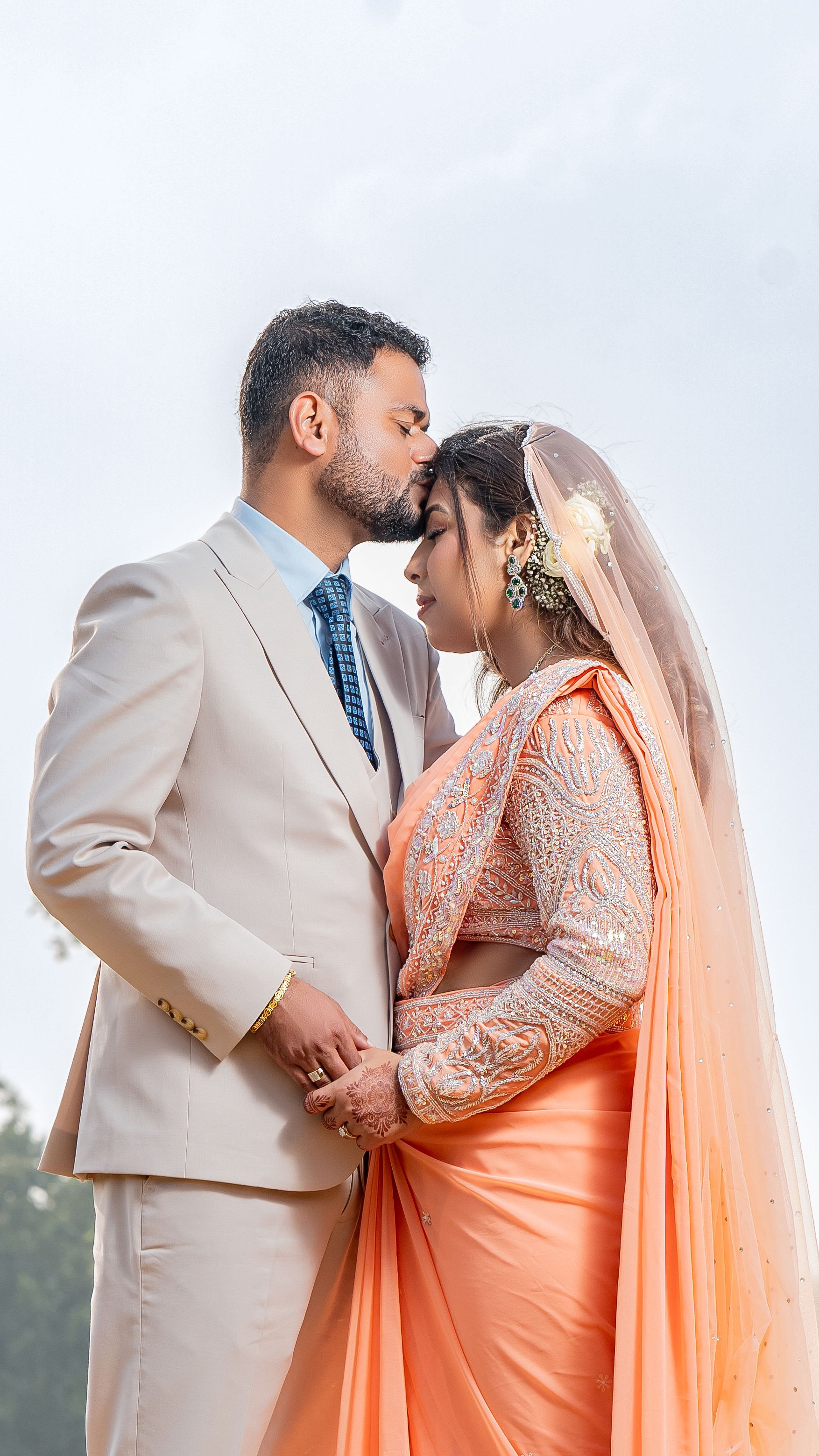 A loving couple in traditional attire sharing an intimate moment outdoors under a clear sky.