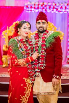 Elegant portrait of a South Asian couple in traditional wedding attire, celebrated with vibrant decor.