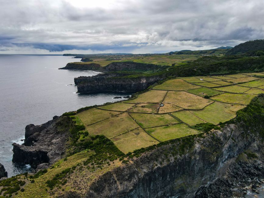 A stunning aerial perspective of patterned farmland along rugged coastal cliffs under a moody sky.