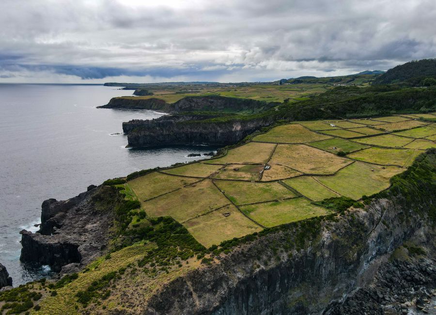 A stunning aerial perspective of patterned farmland along rugged coastal cliffs under a moody sky.